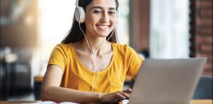 Young woman wearing headphones and smiling while studying on a laptop at a desk.